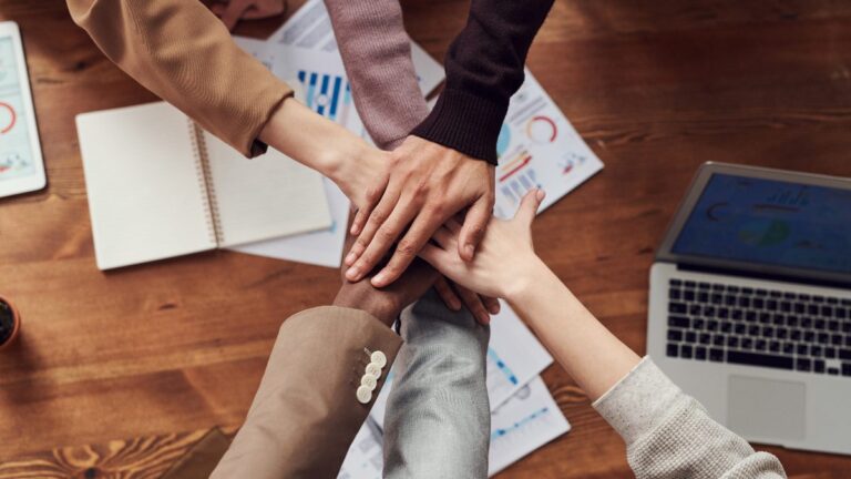 Imagem de um grupo de colegas de trabalho com as mãos juntas, representando a coletividade e um bom clima organizacional na empresa