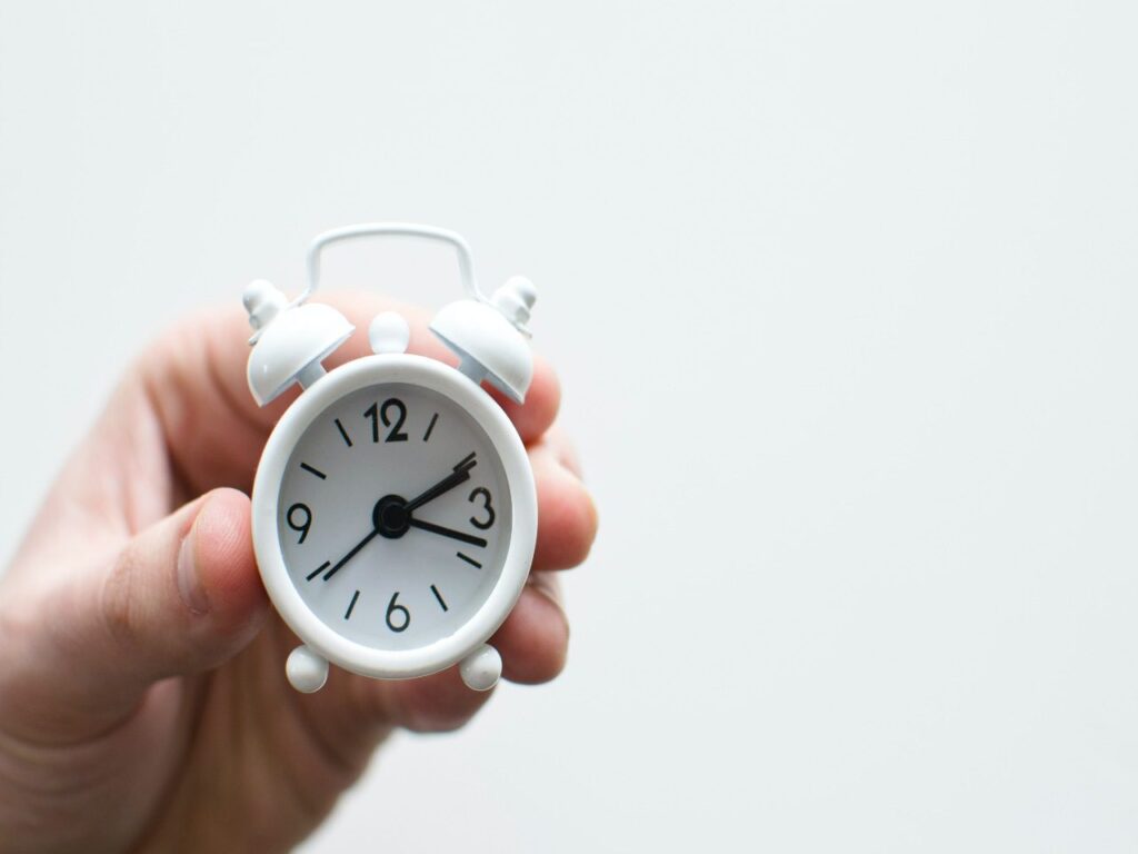 Foto de uma mão segurando um relógio branco para ilustrar um texto sobre horário de almoço