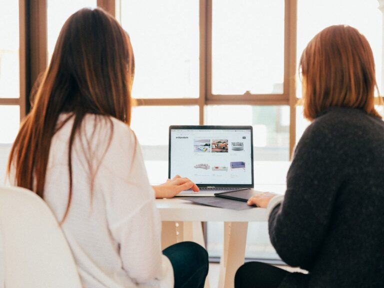 Imagem de duas mulheres sentadas na frente de um computador para ilustrar o texto sobre ferramentas indispensáveis para o setor de Departamento Pessoal