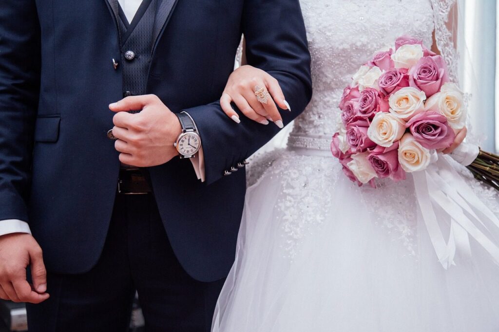 Homem de terno preto e mulher de vestido de noiva segurando um buquê em cerimônia de casamento, ilustrando do que se trata a licença gala ou licença casamento
