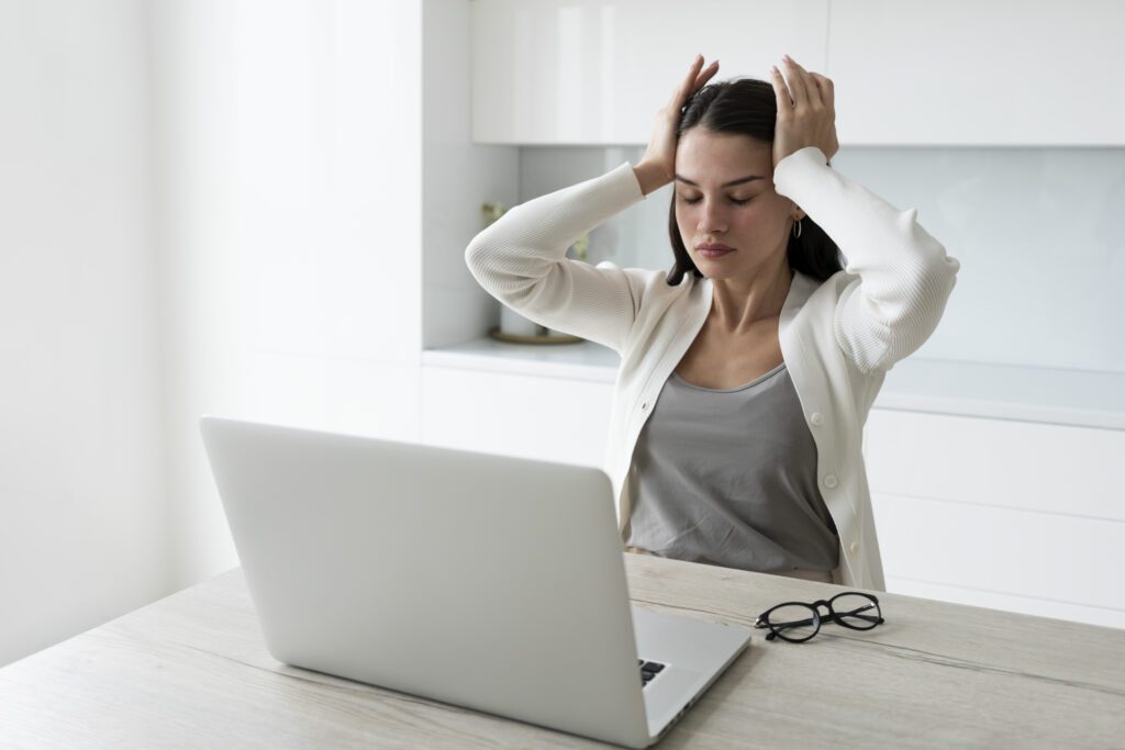 Mulher com as mãos na cabeça em frente a uma mesa com notebook