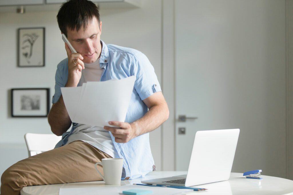 Homem sentado em cima de uma mesa analisando papelada