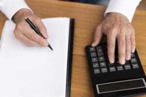 Pessoa fazendo cálculo usando calculadora e papel